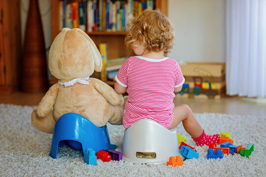 Closeup of cute little 12 months old toddler baby girl child sitting on potty. Kid playing with doll toy. Toilet training concept. Baby learning, development steps