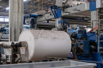 A roll of white fabric in a textile factory in close up view.