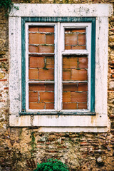 A boarded up with bricks rustic window against squatters with wooden shutters stands against an aged stone wall in a quaint village, showcasing time-worn charm