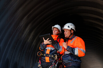 Female and male engineers work inside a large steel pipe. Workers build pipelines to transport oil,...