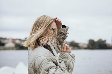 A branch of reeds in the hand of a pretty blond woman near the river, close-up.
