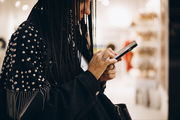Stylish woman with braids using smartphone in public space