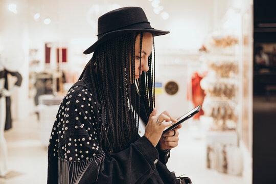 Fashionable woman with braids using smartphone in a boutique