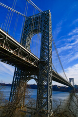 Obraz premium A image of George Washington Bridge against a blue sky. The metal structure spans a river with calm waters, showcasing cityscape views on each side, USA
