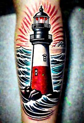  The image shows a tattoo of a lighthouse with the sun rising behind it. The lighthouse is white and red with a black top.