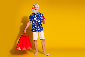 Full body portrait of stylish santa phone bags christmas print shirt shorts isolated on yellow color background