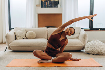 African American woman, sportswoman training at home, sitting in lotus position, leaning to the side