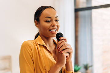 Portrait of young, beautiful African American woman singing, holding microphone, looking away