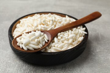 Puffed rice in bowl and spoon on light grey table, closeup