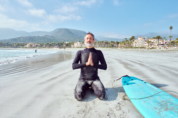 Senior man meditating on the beach before getting into the water to surf the waves