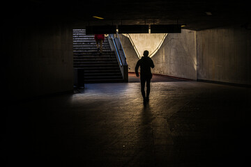 Silhouette of a Person Walking in a Dark Underpass with Sunlit Stairs