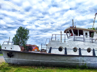 An old ship rests on the shore, showcasing its weathered charm against a backdrop of cloudy skies...