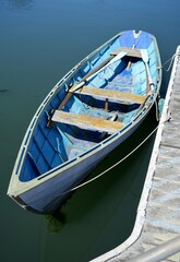 Pastel Blue faded painted rowing boat with oars moored on a wooden pier.