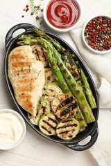 Delicious grilled vegetables and chicken breast in baking dish on white wooden table, flat lay
