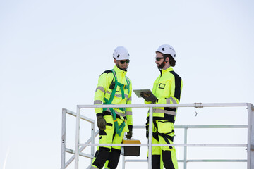 Fototapeta premium Group of male engineer working with plan inspecting or maintenance of wind turbines at windmill field farm. Team of male engineer control or monitoring wind turbine system at wind turbines farm