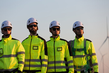 Group of male engineer wearing safety uniform standing together at wind turbines farm. Team of male technician planning maintenance of wind turbines at windmill field farm