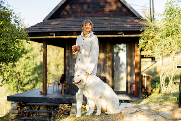 A woman in a cozy fleece jacket enjoys her morning coffee outdoors, standing next to her friendly...