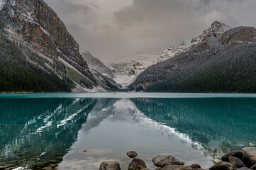 Lake Louise clear calm blue turquoise water smoothly reflecting the image of the mist covered glacier and snowy mountains in the background in Banff National Park during cloudy foggy autumn morning