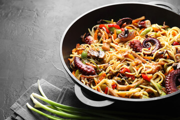 Stir-fry noodles with sea food and vegetables in wok on dark textured table, closeup