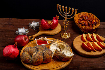 Challah, honey, apple and pomegranate and burning candles on wooden table with menorah Rosh Hashanah