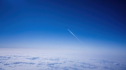 A lone airplane leaves a contrail in the bright blue sky, high above the clouds.