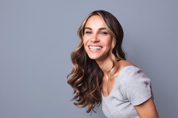 Portrait of young happy woman with a big smile on her face looking camera on a gray