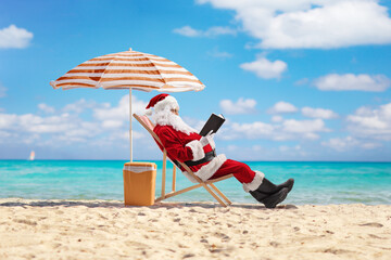 Santa claus reading a book on a sandy beach