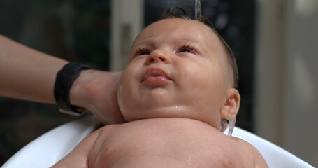 Baby gazing upwards while water is poured during bath, water droplets on face, calm and attentive,...