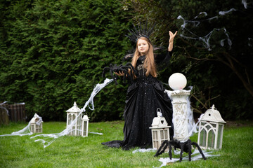 Sorceress European girl 8 years old raises her hand while holding a huge spider black for Halloween