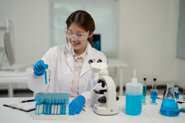 Smiling scientist wearing lab coat and gloves analyzing test tubes with blue liquid in a laboratory...