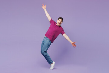 Fototapeta premium Full body young man wear violet t-shirt casual clothes standing on toes dancing lean back have fun spreading hands isolated on plain pastel light purple background studio portrait. Lifestyle concept.
