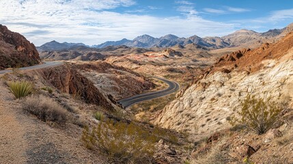 Fototapeta premium A winding road through a mountainous desert landscape under a blue sky.