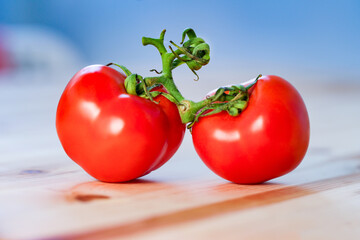 Two red tomatoes with a green twig are lying on the table