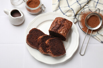 Delicious cut chocolate sponge cake and ingredients on white tiled table, flat lay