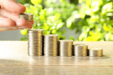 Salary concept. Woman putting coins on stack at grey table, closeup