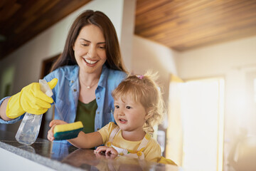 Obraz premium Mother, kid and cleaning table with spray in home for helping hand, teaching hygiene or bonding. Family, woman or girl child with disinfectant to wipe surface in house for bacteria or chores support