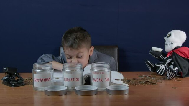 Child in a business suit reading book about finance wit a sceleton money bank and saving jars on the table. Questioning and funny face expression. High quality 4k footage