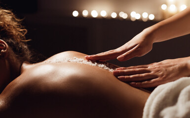African-american woman getting salt scrub treatment in health spa, closeup