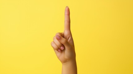 Naklejka premium Woman's index finger points upward on a yellow background. Close-up of the hand.