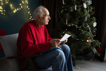 Old man sad holding picture of wife sitting on chair in living room alone on christmas