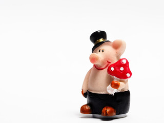 In tis photoillustration Vintage porcelain figurine of pig in a hat and black pants holds a fly agaric on white background