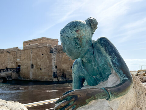 A statue of a woman lying on a rock in front of the castle in Paphos Harbour, Cyprus