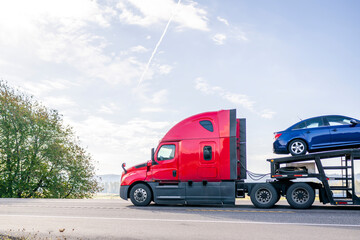 Red high cab big rig car hauler semi truck transporting blue on the modular semi trailer running on...