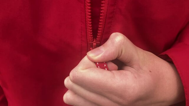 A young man unzipping his red jacket. Slow motion. Close up.