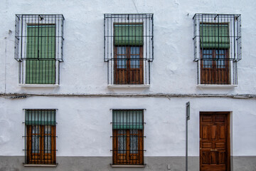 Obraz premium Elongated windows with typical la mancha bars and wooden door on the facade of a white house in Ocaña, province of Toledo. Spain