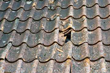 Damage to the clay tile roof of a historic house with some roof tiles missing, broken roof tiles