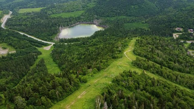 Drone aerial view of Val d'Ir&egrave;ne Regional Park in summer with vibrant green ski runs, a winding mountain trail without snow and Lake Joram near Sainte-Ir&egrave;ne in Matapedia Valley, Quebec, Canada.