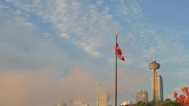 scenic view of the Canadian flag waving proudly with Skylon Tower in background, set against sky of soft clouds.Canadian flag concept patriotism, tourism, and architecture. Canadian flag Skylon Tower.