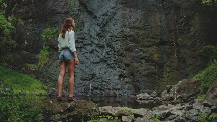 Woman enjoying a waterfall view in nature, perfect for adventure seekers. A serene setting for exploration in the outdoors