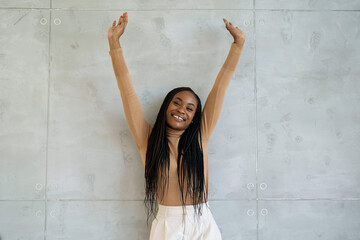 A cheerful black businesswoman stretches her arms high with a radiant smile, dressed in...